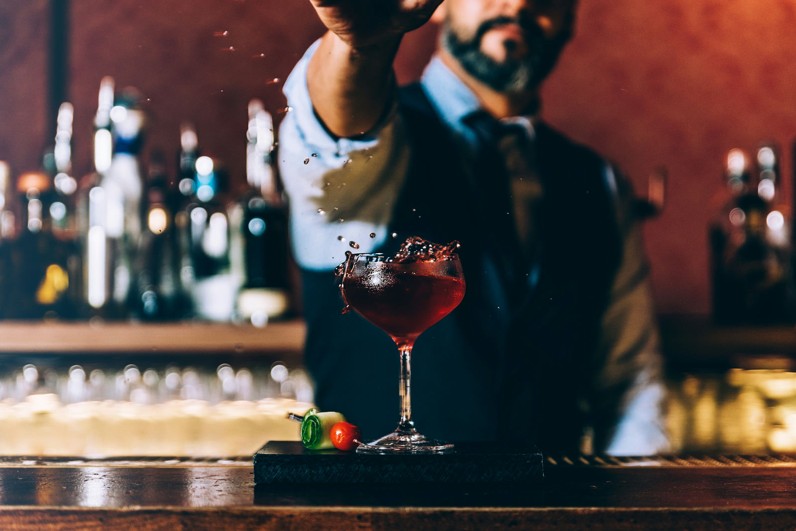 A bartender prepares a red cocktail behind a warmly lit event bar.
